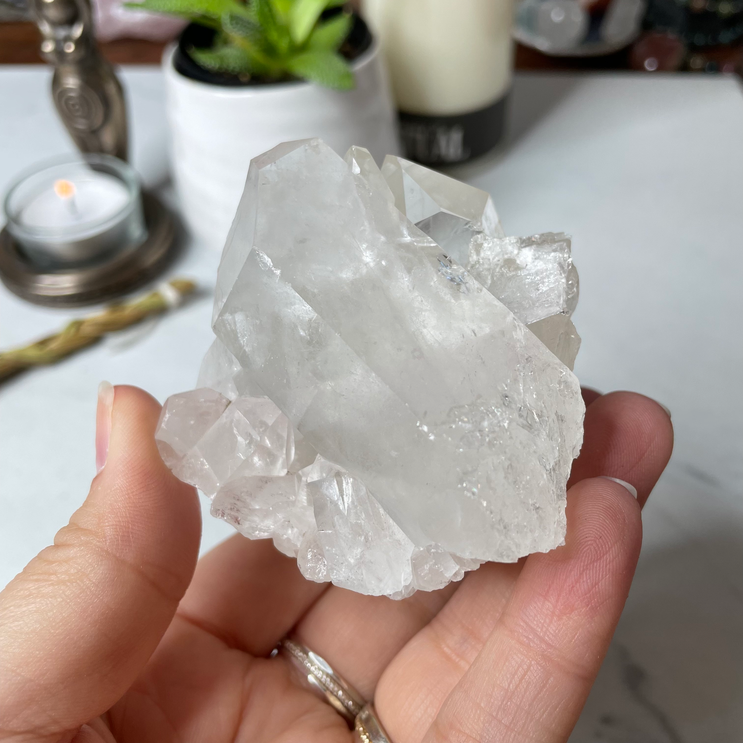 Freya's Haven | Metaphysical & Crystal shop | A close up photo of a Clear Quartz Cluster held in a woman's hand with candles in the background.