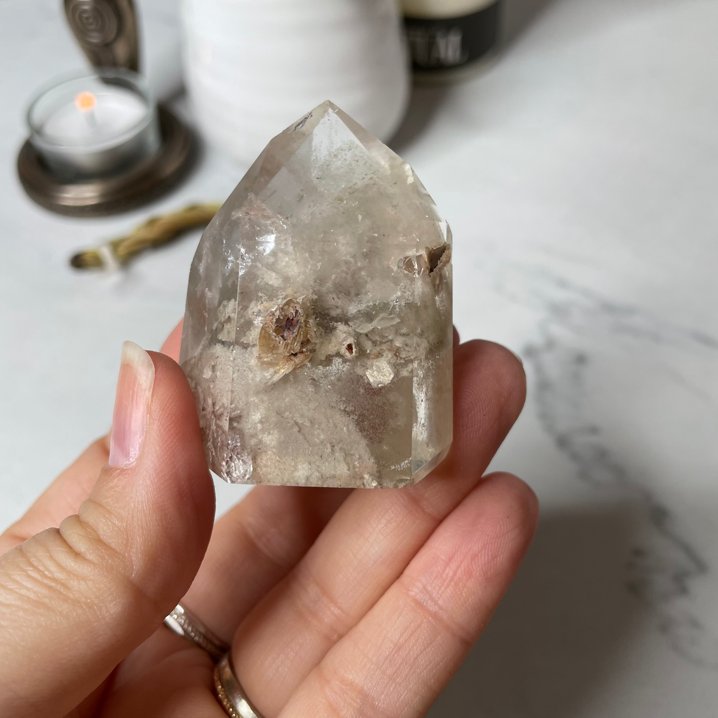 Freya's Haven | Metaphysical & Crystal shop | A close up photo of  a Lodalite  crystal held in a woman's hand with candles in the background.