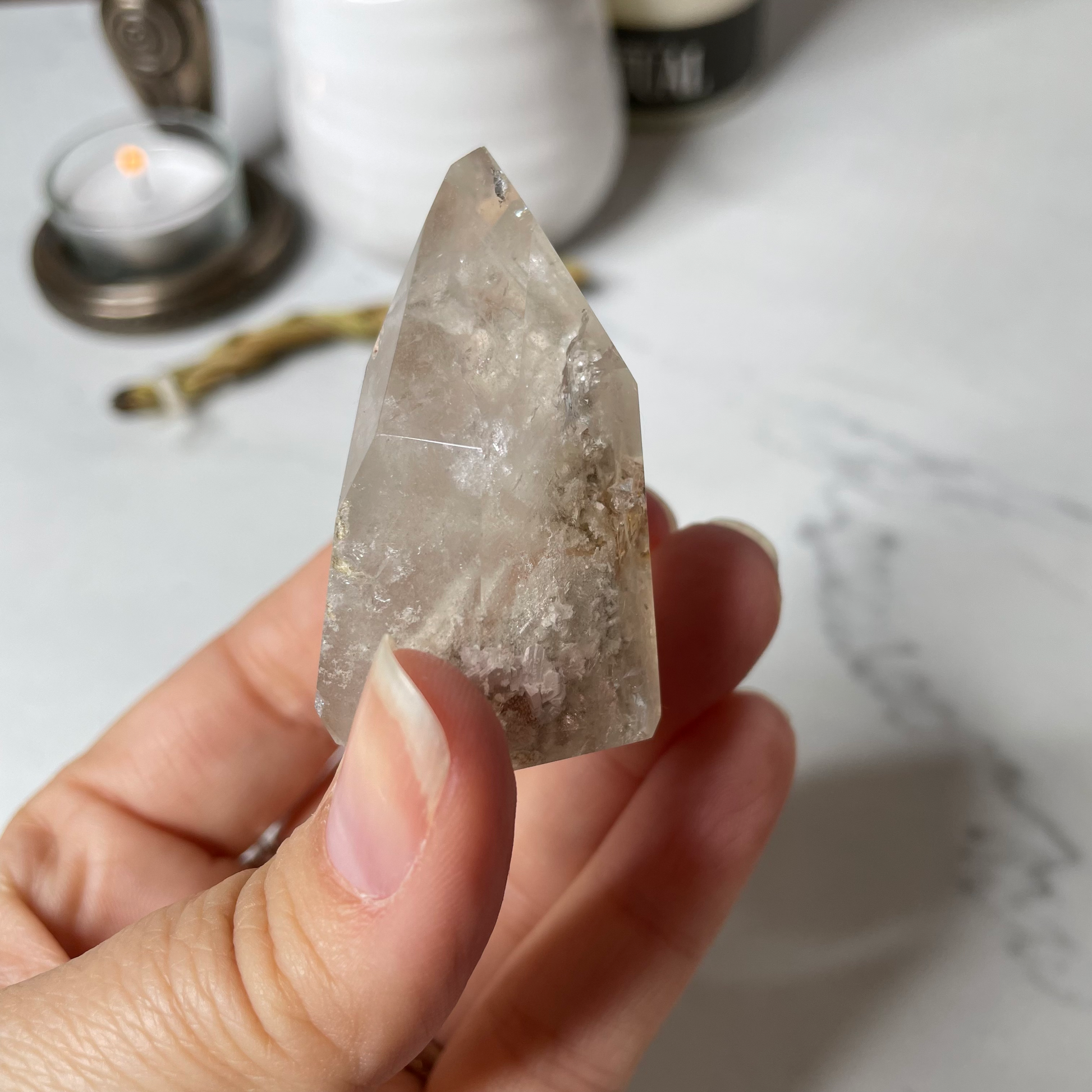 Freya's Haven | Metaphysical & Crystal shop | A close up photo of  a Lodalite  crystal held in a woman's hand with candles in the background.