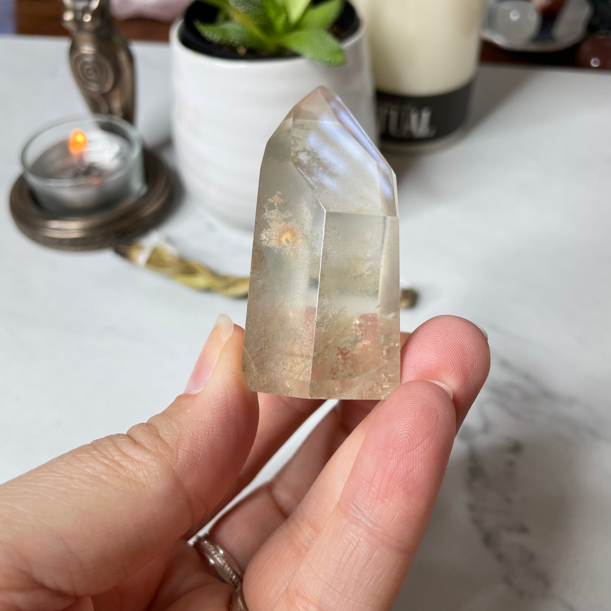 Freya's Haven | Metaphysical & Crystal shop | A close up photo of a Citrine Phantom tower held in a woman's hand with candles in the background.