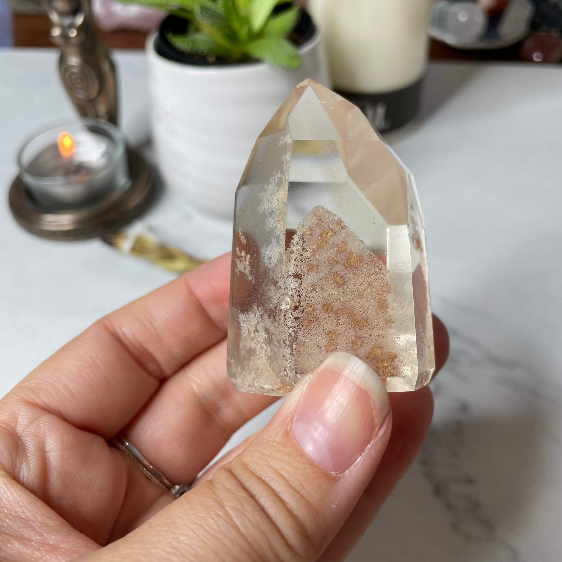 Freya's Haven | Metaphysical & Crystal shop | A close up photo of a Citrine Phantom tower held in a woman's hand with candles in the background.