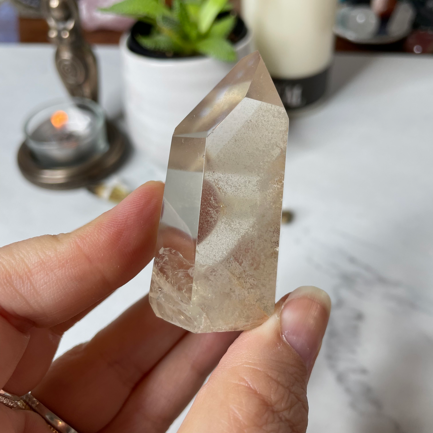 Freya's Haven | Metaphysical & Crystal shop | A close up photo of a Citrine Phantom tower held in a woman's hand with candles in the background.