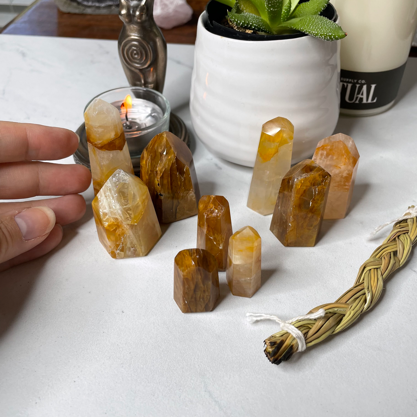 Freya's Haven | Metaphysical & Crystal shop | A close up photo of a Golden Healer tower held in a woman's hand with candles in the background.