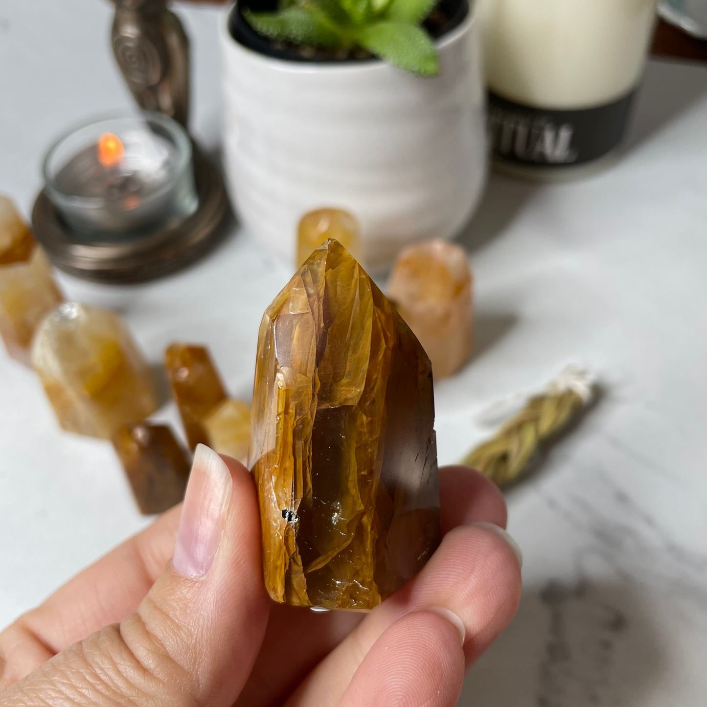 Freya's Haven | Metaphysical & Crystal shop | A close up photo of a Golden Healer tower held in a woman's hand with candles in the background.