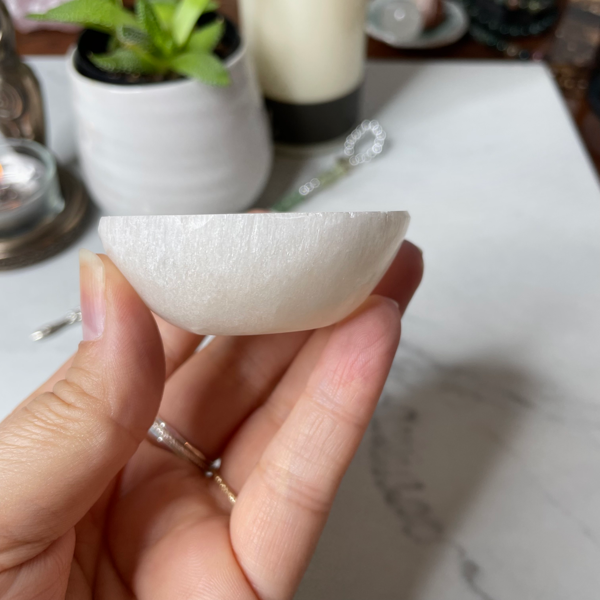 Freya's Haven | Metaphysical & Crystal shop | A close up photo of an orange Selenite bowl held in a woman's hand with candles in the background.
