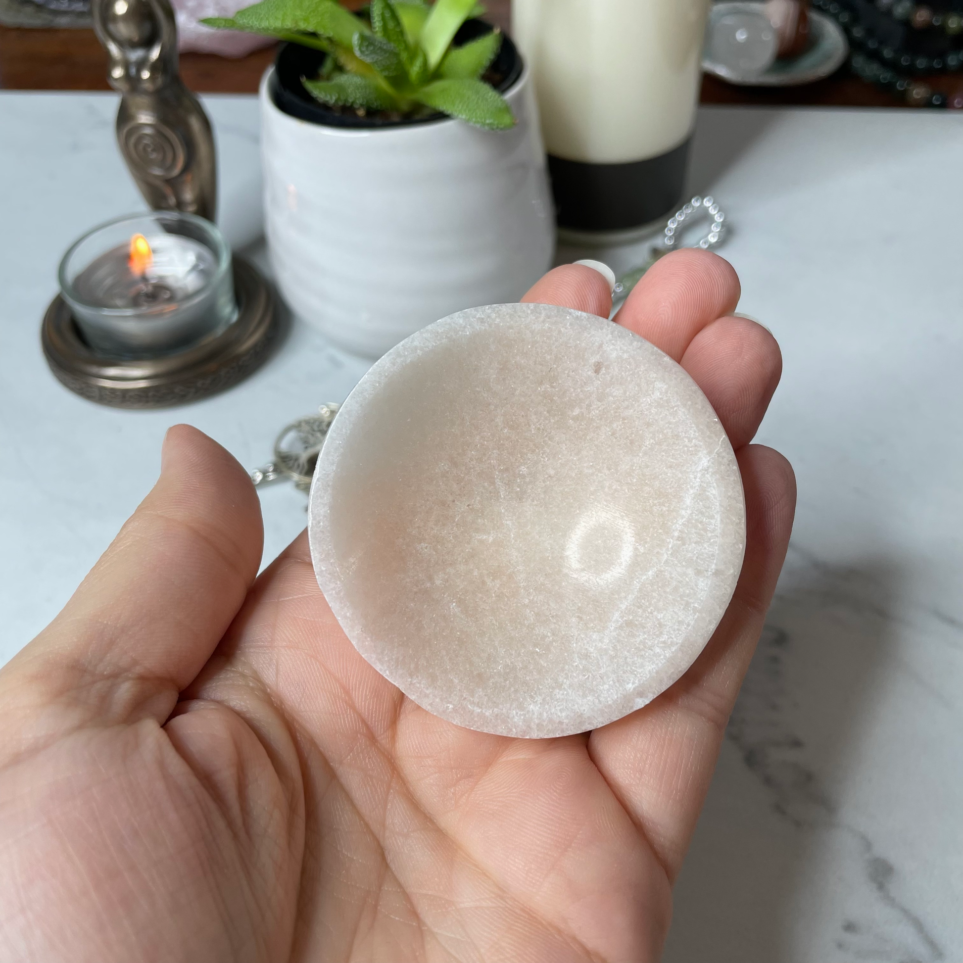 Freya's Haven | Metaphysical & Crystal shop | A close up photo of an orange Selenite bowl held in a woman's hand with candles in the background.