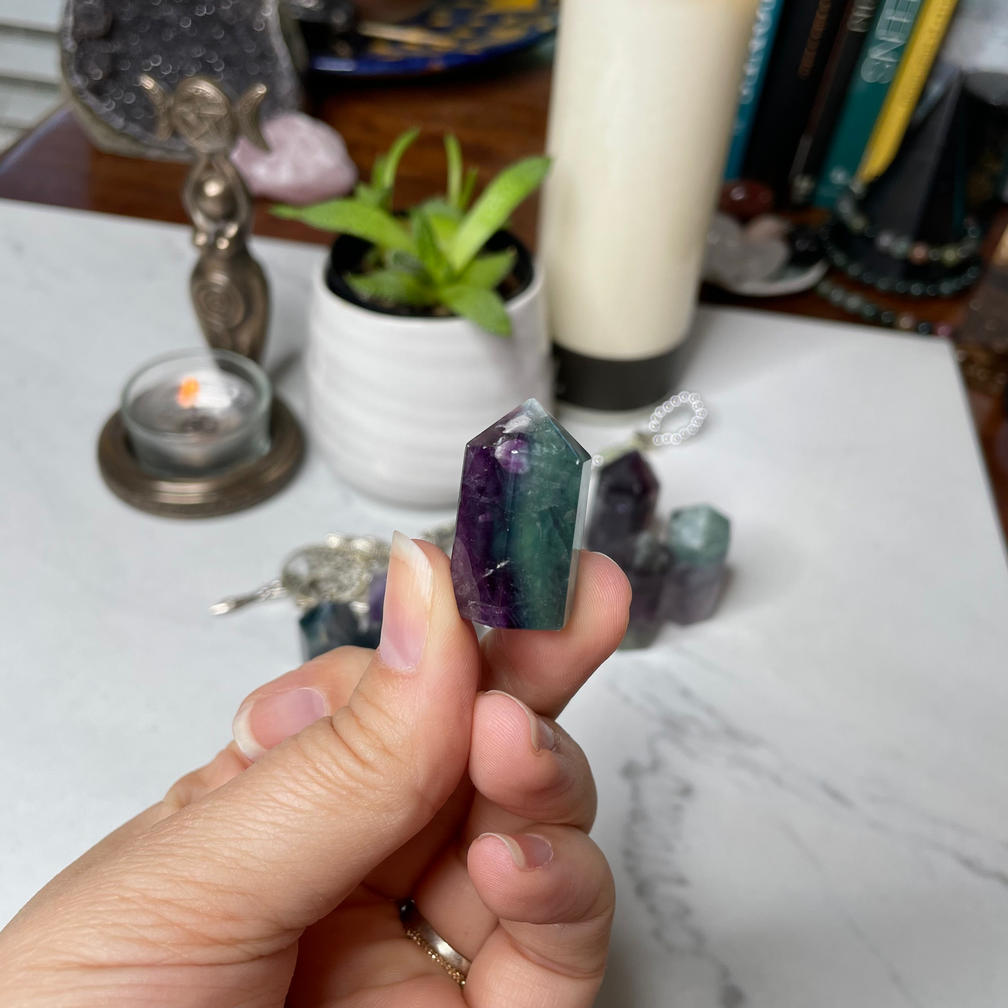 Freya's Haven | Metaphysical & Crystal shop | A close up photo of  a Rainbow Fluorite tower held in a woman's hand with candles in the background.