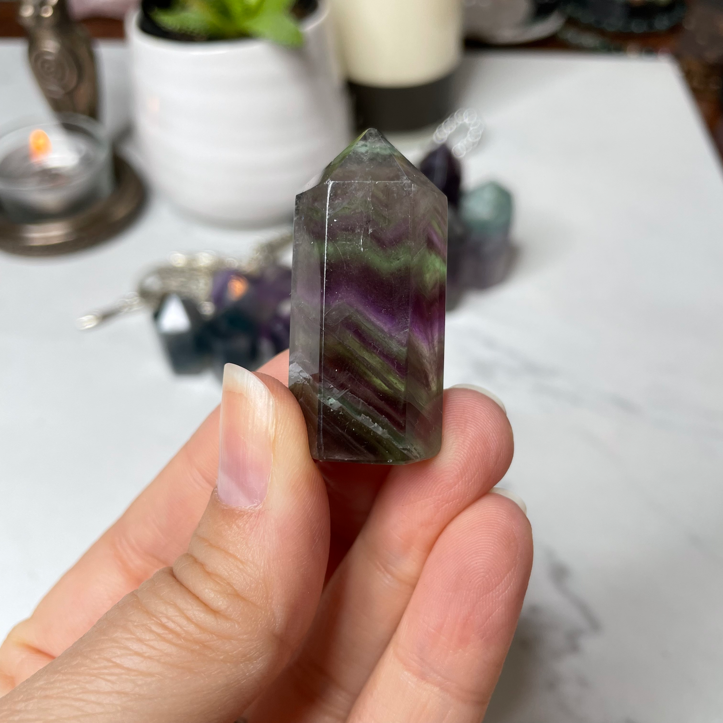 Freya's Haven | Metaphysical & Crystal shop | A close up photo of  a Rainbow Fluorite tower held in a woman's hand with candles in the background.