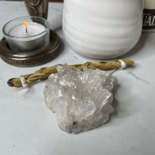 Freya's Haven | Metaphysical & Crystal shop | A close up photo of a Clear Quartz Cluster held in a woman's hand with candles in the background.