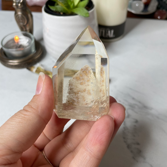 Freya's Haven | Metaphysical & Crystal shop | A close up photo of a Citrine Phantom tower held in a woman's hand with candles in the background.